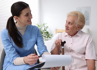 Obraz premium Nurse with clipboard examining senior woman indoors. Home health care service