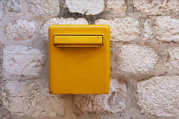 Yellow metal mailbox on a stone wall. Empty copy space