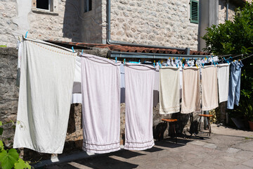 Beige towels and linens hang to dry on a clothesline in the courtyard of an old house.