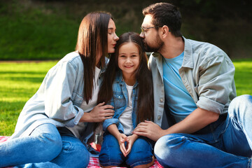Family portrait of parents kissing their happy daughter in park