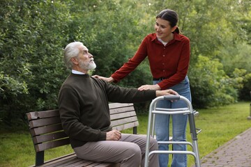 Smiling caregiver supporting elderly man with walking frame outdoors