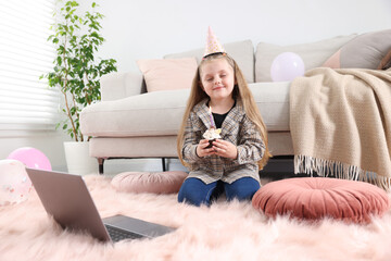 Birthday celebration. Little girl with cupcake having video call via laptop at home