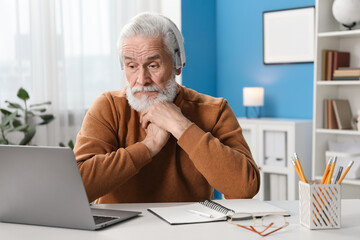 Senior man learning online using laptop at desk indoors. Self-study