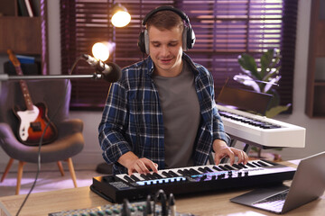 Man in headphones working with MIDI keyboard at table in home studio