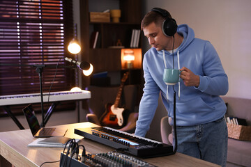 Man in headphones working with MIDI keyboard at table in home studio