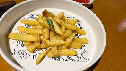 This image features a white bowl filled with golden-brown french fries, lightly seasoned with herbs, resting on a paper liner with playful doodles