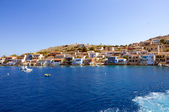 A scenic view of the harbor in the small town of Halki, showing colorful boats gently floating on crystal-clear turquoise water