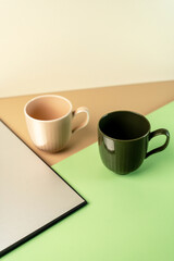 Two empty ribbed ceramic mugs, dark green and beige, arranged on a modern geometric background of green, beige, and grey. Stylish tableware concept.