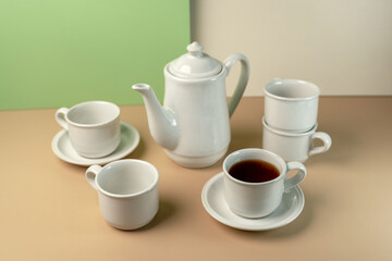 White ceramic tea set with a teapot and stackable cups. One cup is filled with black tea. Clean, minimalist still life with copy space.