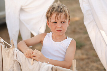 Young boy hanging laundry on outdoor clothesline with wooden clothespins. Sunny countryside...