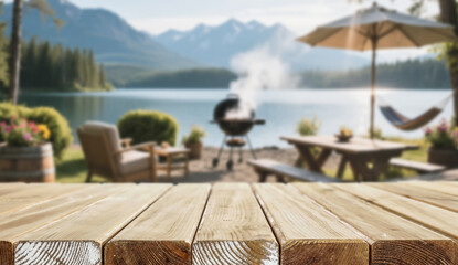 Wooden table with space for product in front of barbecue by the lake – summer camping and outdoor cooking concept. Blurred background of calm lake with distant mountains and a clear blue sky.