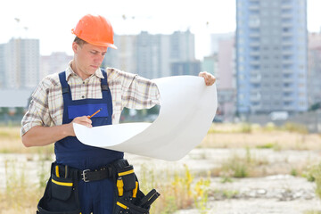 Looking at blueprints in a building site. Man builder in hardhats with clipboard and blueprint on outdoors. Construction worker holding a circuit structure of the plan. Worker on a construction site.