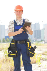Male builder with electronic tablet in hands. Seating is on a new construction site. Male construction engineer with touch pad and checking building and site construction. Get important message.