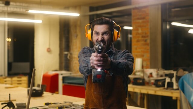 Expressive Caucasian handyman man wood master drilling electric instrument carpenter holding drill in workshop aggressive craftsman guy repairing male using power tool repairman builder woodworking