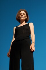 A woman in black outfit poses against a vibrant blue sky, looking straight at the camera.