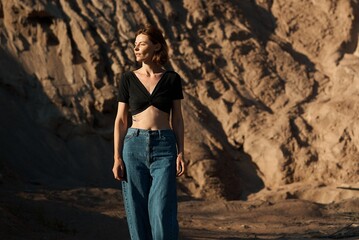 Naklejka premium A stylish woman poses confidently in a black top and jeans outdoors.