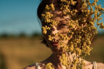 Woman's face peeking through vibrant yellow flowers in soft sunlight, evoking peace.