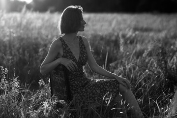 A woman in a floral dress sits pensively in a sunlit field, enjoying a moment of peace.
