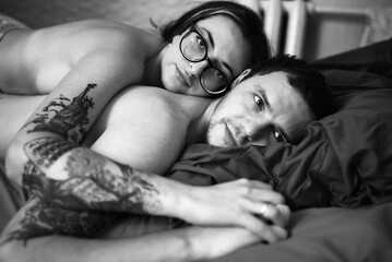 An intimate black and white portrait of a loving couple lying in bed together.
