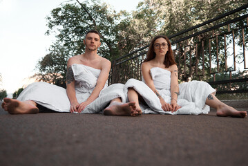 A couple wrapped in white blankets sit on a road, creating a peaceful and intimate scene.