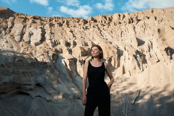 A woman stands before a stunning sandstone cliff, bathed in sunlight with a serene look.