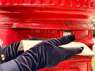 Postman standing by iconic red post box on British street in daylight