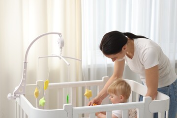 Mother playing with her cute baby in crib at home