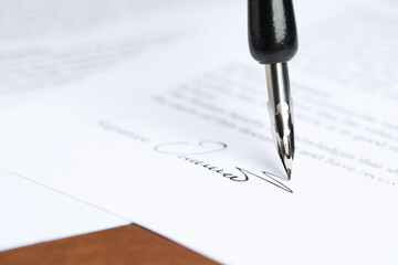Signing notary document with fountain pen at brown table, closeup