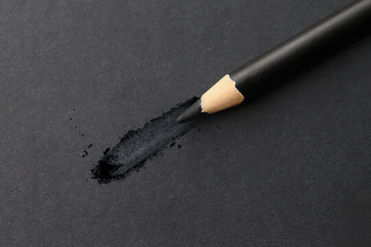 Close up of black charcoal graphite pencil on dark paper surface with black drawn hatching. Koyal eye pencil