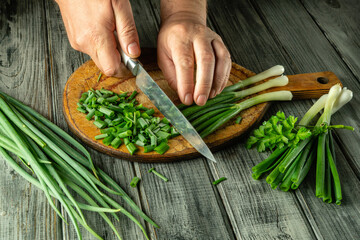 Hands skillfully chop scallions on a wooden board, surrounded by fresh green onions and herbs in a warm, rustic kitchen during daylight hours