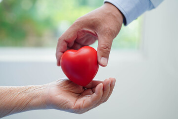 Asian elder senior woman patient holding red heart in hospital.