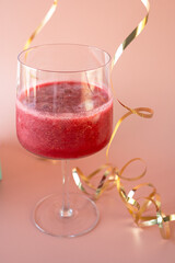 Festive Celebration: Red Cocktail with Gold Streamers. Composition featuring a glass filled with a vibrant red cocktail against a soft blush pink background, complemented by festive gold streamers