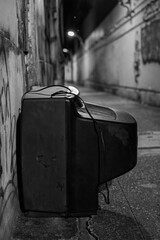 Old cathode ray tube television discarded in narrow Bangkok alleyway at night with overhead lights