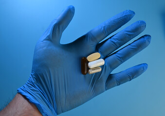 hand in blue medical glove holding several pills
