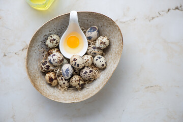 Bowl with raw quail eggs on a light-beige marble background, horizontal shot with space, above view