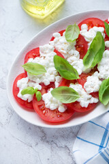 Caprese with cottage cheese, red tomato slices and fresh green basil, vertical shot on a white stone background, middle close-up