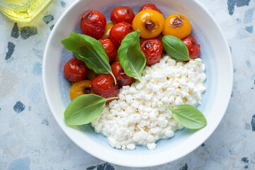 Plate with cottage cheese, roasted cherry tomatoes and fresh green basil, horizontal shot, elevated view, middle close-up