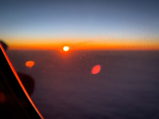 Bright sunset above the clouds seen through an aircraft window with visible lens flare and window reflections