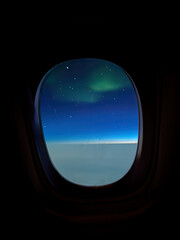 Aurora borealis northern lights seen from an airplane window at night, glowing above a blanket of clouds against a blue sky with stars
