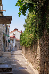 Narrow stone alley leading to a white house with a red roof, surrounded by greenery. Bright summer...