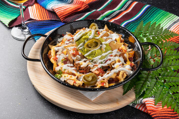 Delicious nachos with guacamole, jalapeños, sour cream and cheese sauce in black pan