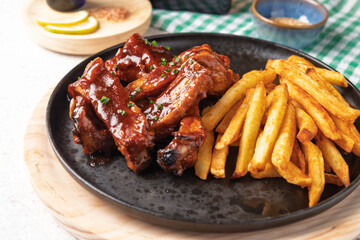 Delicious bbq pork ribs with crispy french fries on black plate