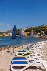 Folded blue umbrellas and sun loungers on a quiet beach with turquoise water. Vertical shot with blue sky space for text overlay.
