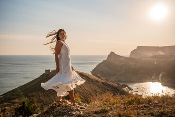 A woman in a white dress stands on a hill overlooking the ocean. The scene is serene and peaceful,...