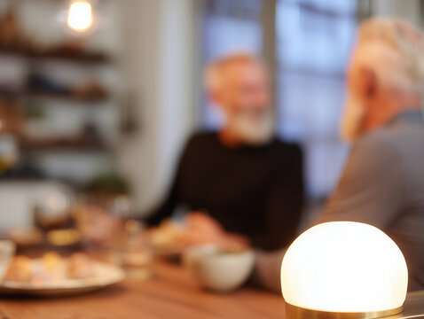 Round smart lamp illuminating wooden table with blurred father and son talking in background - Powered by Adobe