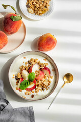 Natural greek yogurt with granola or muesli, peach and mint in a bowl on a white background