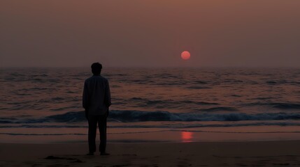 Silhouette of man standing alone on beach watching dramatic red sunset over ocean waves, moody atmospheric seascape with dark tones and reflection on wet sand.