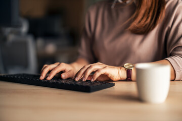 Woman Typing at Keyboard with Coffee Mug on Desk