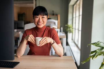 Smiling Woman Enjoying Coffee at Modern Office Desk