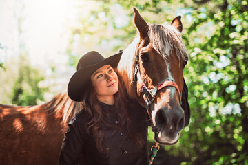 woman cowgirl, stands next to her horse in summer season